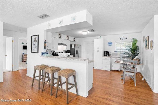 202 Monroe Ave, Cape Canaveral, FL 32920 - kitchen featuring white cabinetry, stainless steel fridge with ice dispenser, a textured ceiling, light wood-type flooring, and kitchen peninsula