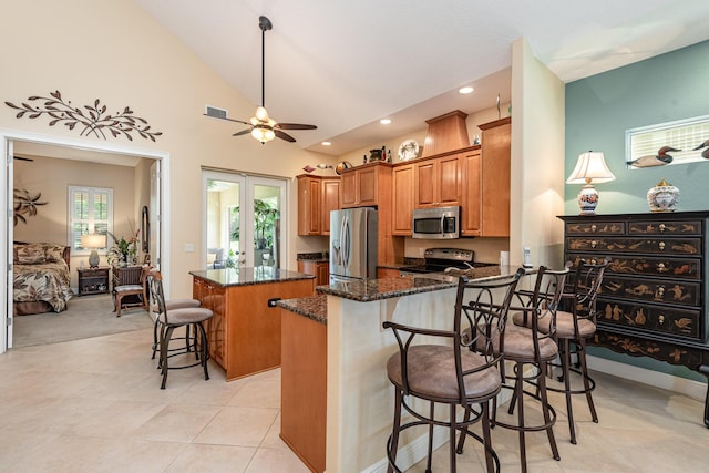 kitchen with kitchen peninsula, appliances with stainless steel finishes, dark stone counters, a center island, and a breakfast bar area