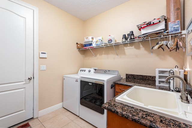 clothes washing area with washing machine and dryer, sink, light tile patterned floors, and a textured ceiling