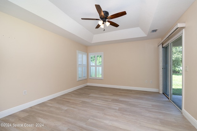 spare room featuring light hardwood / wood-style floors, a tray ceiling, and ceiling fan