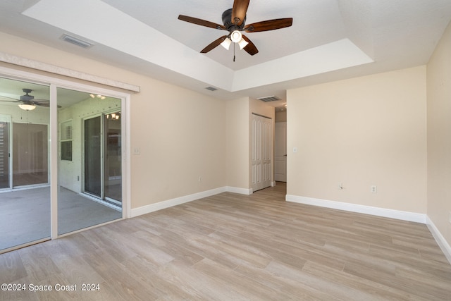 unfurnished room featuring light hardwood / wood-style floors, ceiling fan, and a tray ceiling