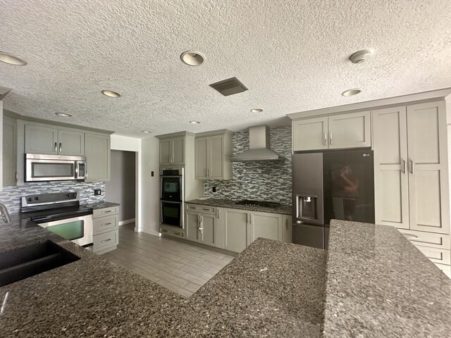 kitchen featuring wall chimney range hood, a textured ceiling, backsplash, and stainless steel appliances