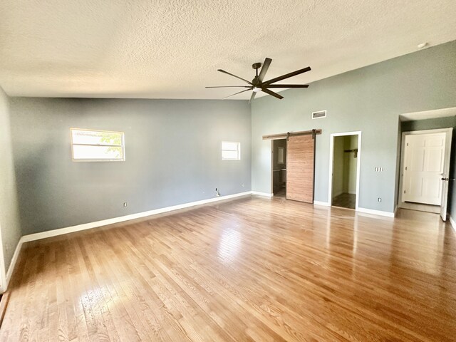 unfurnished bedroom featuring a textured ceiling, hardwood / wood-style flooring, a barn door, high vaulted ceiling, and ceiling fan