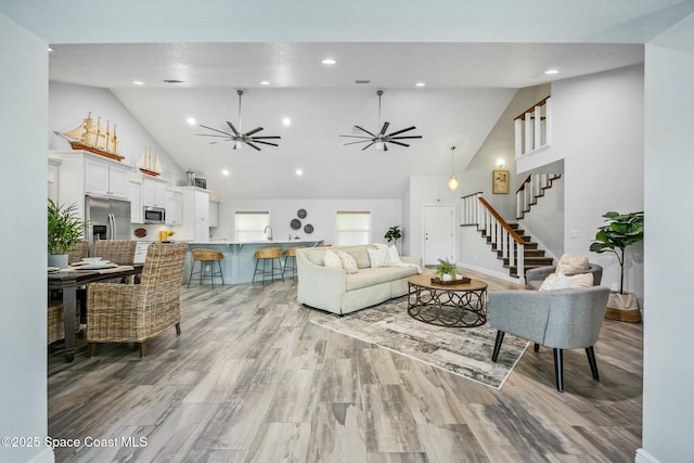 living area featuring high vaulted ceiling, recessed lighting, a ceiling fan, light wood-style floors, and stairs