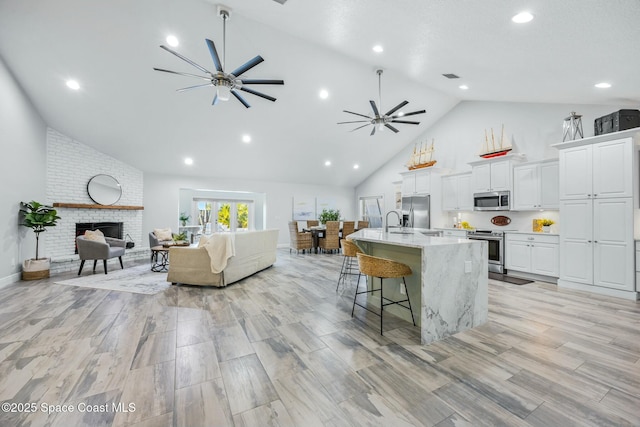 kitchen featuring a ceiling fan, an island with sink, appliances with stainless steel finishes, open floor plan, and a kitchen bar