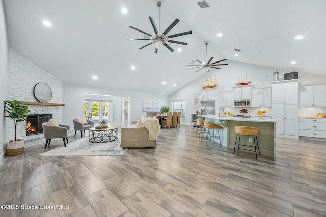 living room with high vaulted ceiling, recessed lighting, visible vents, a ceiling fan, and a brick fireplace