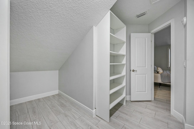 additional living space featuring wood tiled floor, visible vents, a textured ceiling, and baseboards