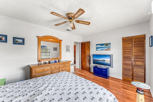 bedroom with ceiling fan, light hardwood / wood-style flooring, a textured ceiling, and a closet