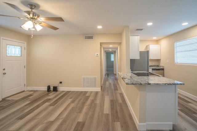 kitchen with light stone countertops, appliances with stainless steel finishes, kitchen peninsula, hardwood / wood-style floors, and white cabinetry