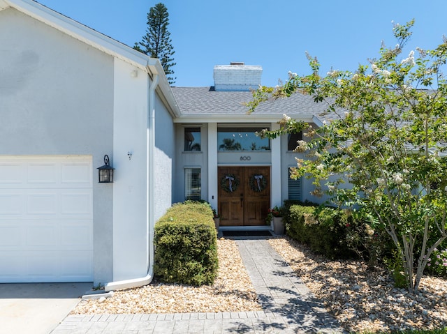 property entrance featuring a garage, a shingled roof, a chimney, and stucco siding