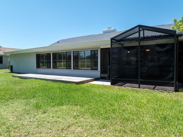 rear view of property with a patio area, glass enclosure, a yard, and a chimney