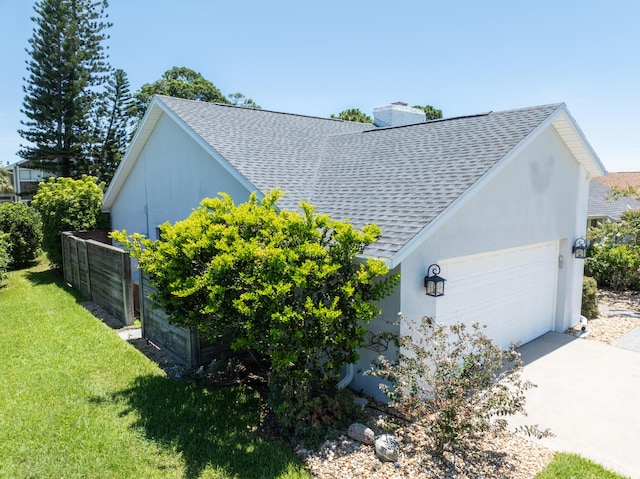 view of side of home featuring a garage, a shingled roof, concrete driveway, a chimney, and a yard