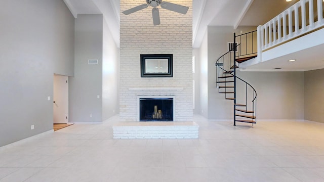 unfurnished living room featuring ceiling fan, a brick fireplace, a towering ceiling, and baseboards