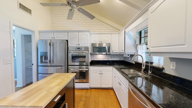 kitchen with appliances with stainless steel finishes, butcher block countertops, a sink, and white cabinetry