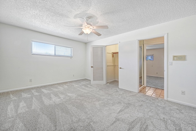 unfurnished bedroom with ceiling fan, a spacious closet, a textured ceiling, light carpet, and a closet