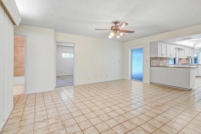 unfurnished living room with ceiling fan, light tile patterned floors, and a textured ceiling