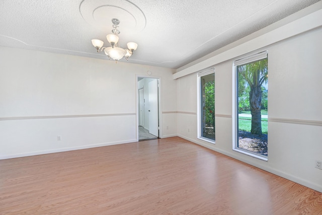 unfurnished room with wood-type flooring, a textured ceiling, and an inviting chandelier