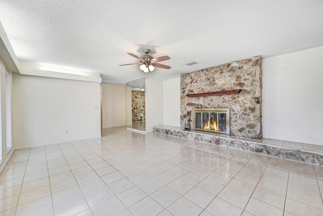 unfurnished living room featuring light tile patterned floors, a textured ceiling, a stone fireplace, and ceiling fan