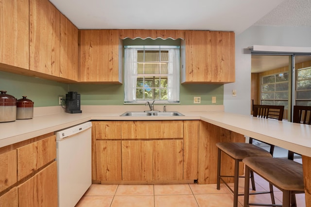 kitchen featuring dishwasher, light tile patterned floors, sink, and a breakfast bar area