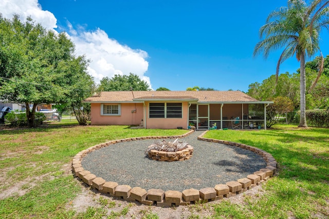 back of property featuring a sunroom, a yard, and a fire pit