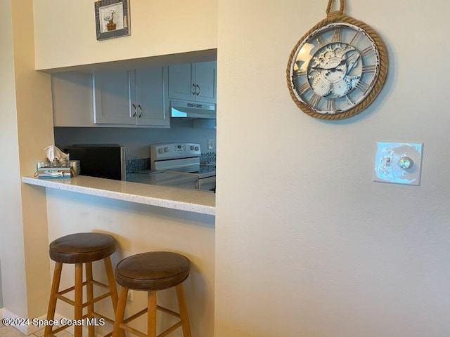 kitchen with electric range oven, a breakfast bar, and light stone countertops