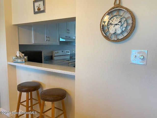7520 Ridgewood Ave Unit 507, Cape Canaveral, FL 32920 - kitchen featuring white range with electric cooktop, under cabinet range hood, a breakfast bar area, and light countertops