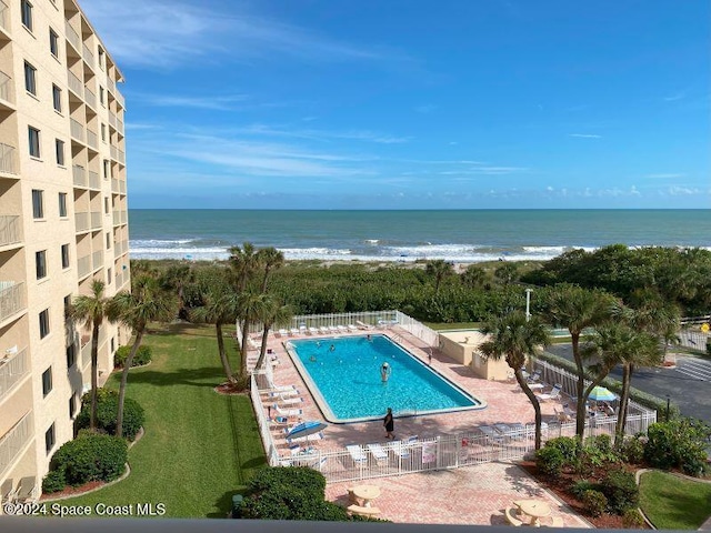 view of swimming pool featuring a beach view, a patio, a water view, and a lawn