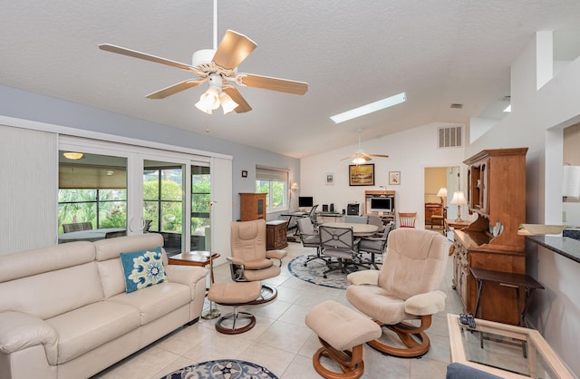 living room featuring lofted ceiling with skylight, light tile patterned floors, a textured ceiling, and ceiling fan