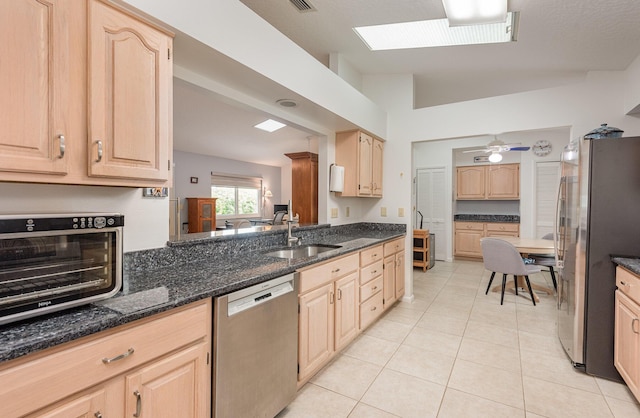 kitchen with appliances with stainless steel finishes, light brown cabinetry, sink, and dark stone counters