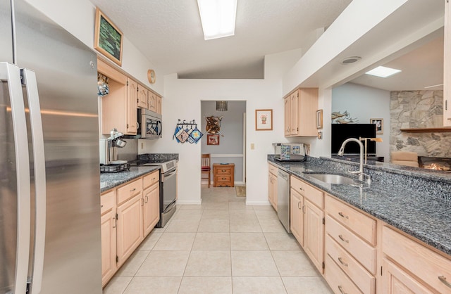 kitchen with appliances with stainless steel finishes, sink, light brown cabinetry, and dark stone counters