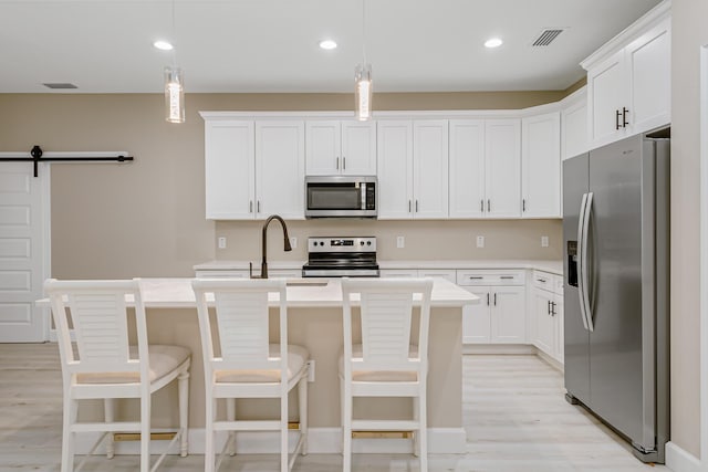 kitchen with white cabinetry, pendant lighting, stainless steel appliances, a barn door, and a kitchen island with sink