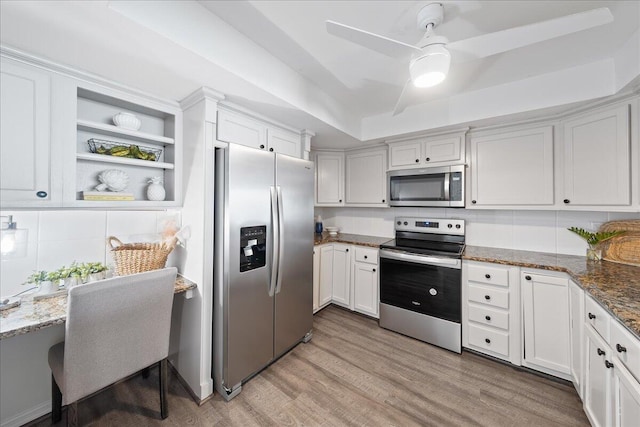 kitchen with appliances with stainless steel finishes, a tray ceiling, decorative backsplash, ceiling fan, and wood-type flooring