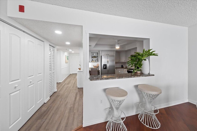 kitchen with stainless steel fridge, wood-type flooring, kitchen peninsula, and a textured ceiling