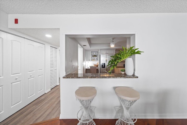 kitchen featuring dark stone counters, white cabinetry, wood-type flooring, a kitchen bar, and stainless steel fridge