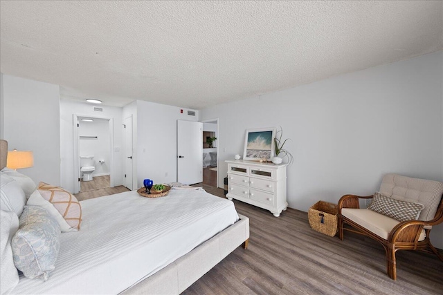 bedroom with a textured ceiling, ensuite bath, and wood-type flooring