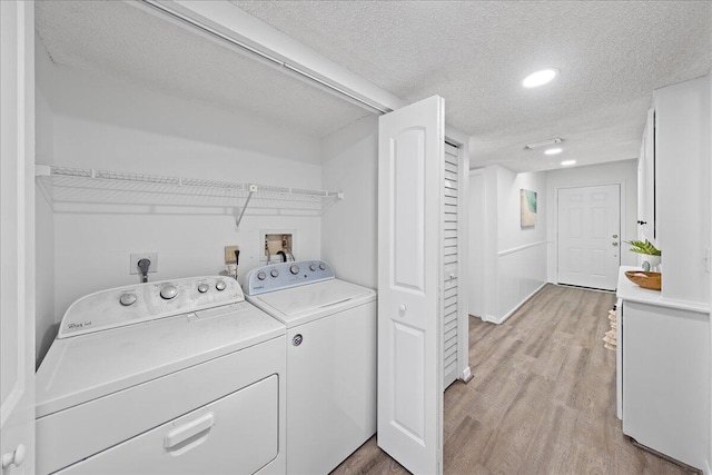 clothes washing area featuring light hardwood / wood-style floors, washing machine and dryer, and a textured ceiling