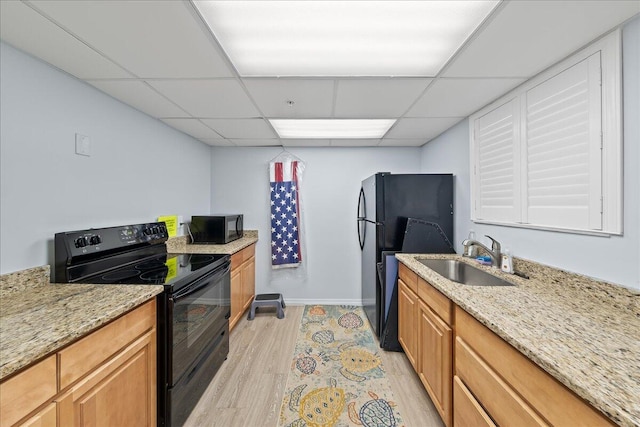 kitchen with black appliances, sink, light stone countertops, a paneled ceiling, and light hardwood / wood-style floors