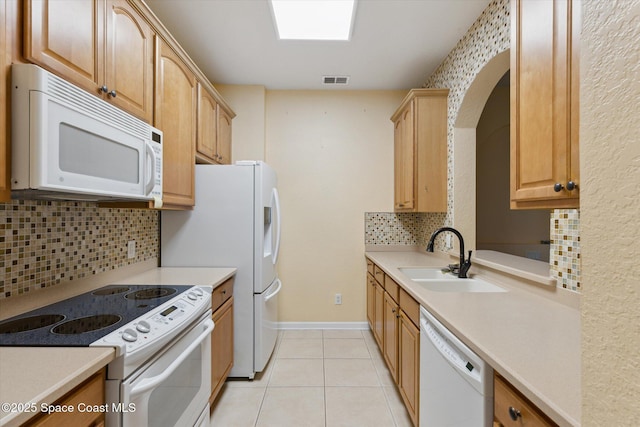 kitchen with a skylight, tasteful backsplash, sink, light tile patterned floors, and white appliances