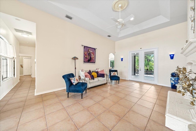 sitting room with ceiling fan, french doors, a raised ceiling, a towering ceiling, and light tile patterned floors