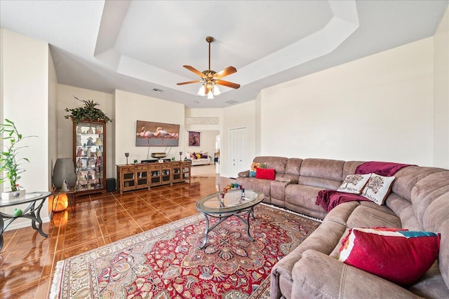 living room featuring ceiling fan, a raised ceiling, and tile patterned flooring