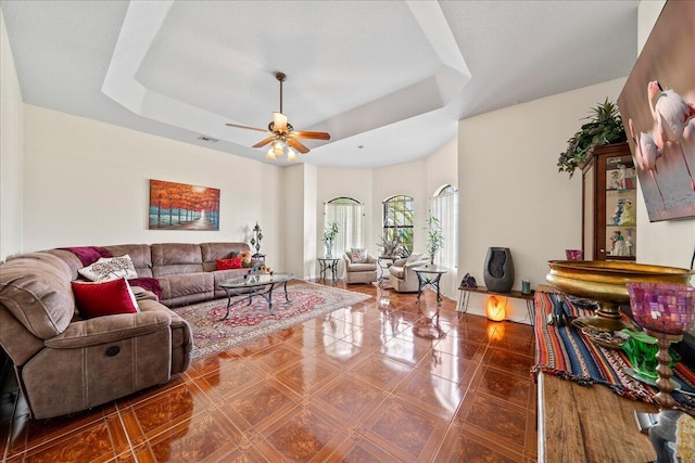 tiled living room with ceiling fan and a tray ceiling