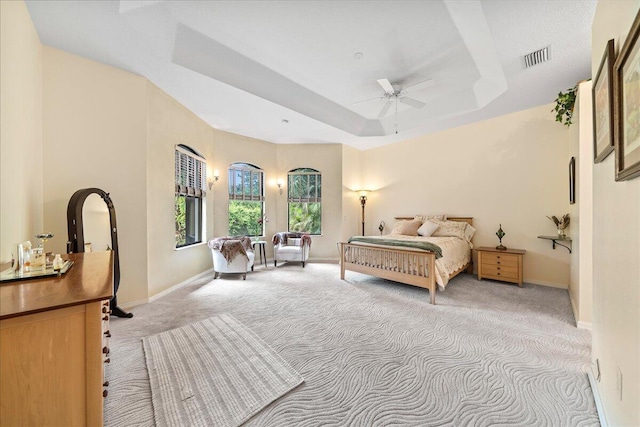 bedroom featuring ceiling fan, a tray ceiling, and light carpet