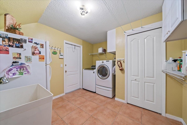 clothes washing area with sink, light tile patterned floors, cabinets, a textured ceiling, and washer and clothes dryer