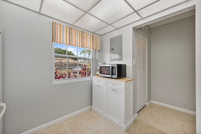 kitchen featuring electric panel, a paneled ceiling, white cabinets, and light tile patterned floors