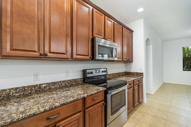 kitchen with light tile patterned flooring, appliances with stainless steel finishes, and dark stone counters