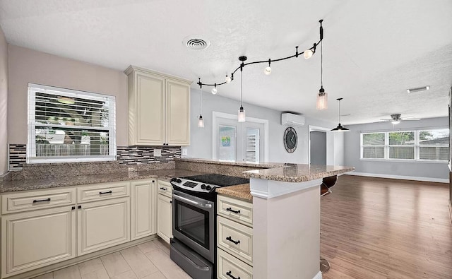 kitchen with pendant lighting, cream cabinets, stainless steel electric stove, ceiling fan, and a wall mounted AC