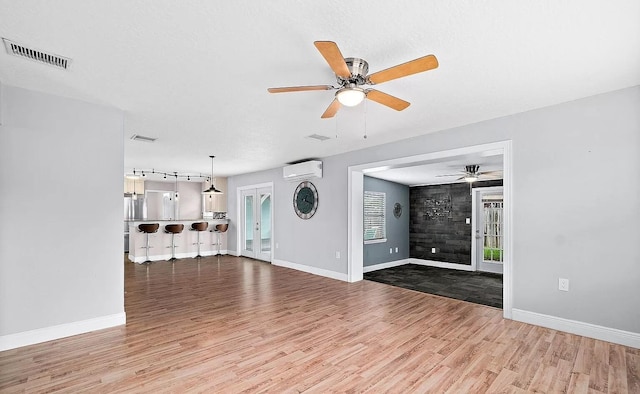 unfurnished living room with hardwood / wood-style floors, ceiling fan, and a wall mounted AC