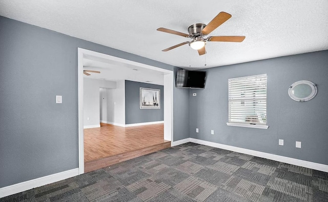 spare room featuring ceiling fan, dark carpet, and a textured ceiling