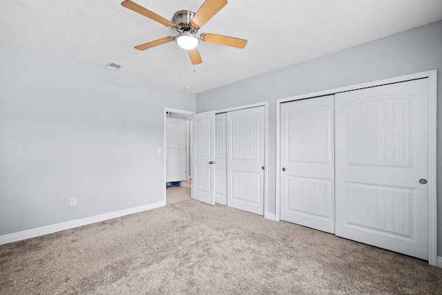 unfurnished bedroom featuring a textured ceiling, ceiling fan, light colored carpet, and two closets