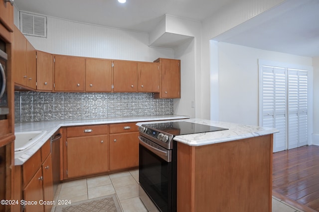 kitchen with black range with electric stovetop, sink, tasteful backsplash, a center island, and light wood-type flooring